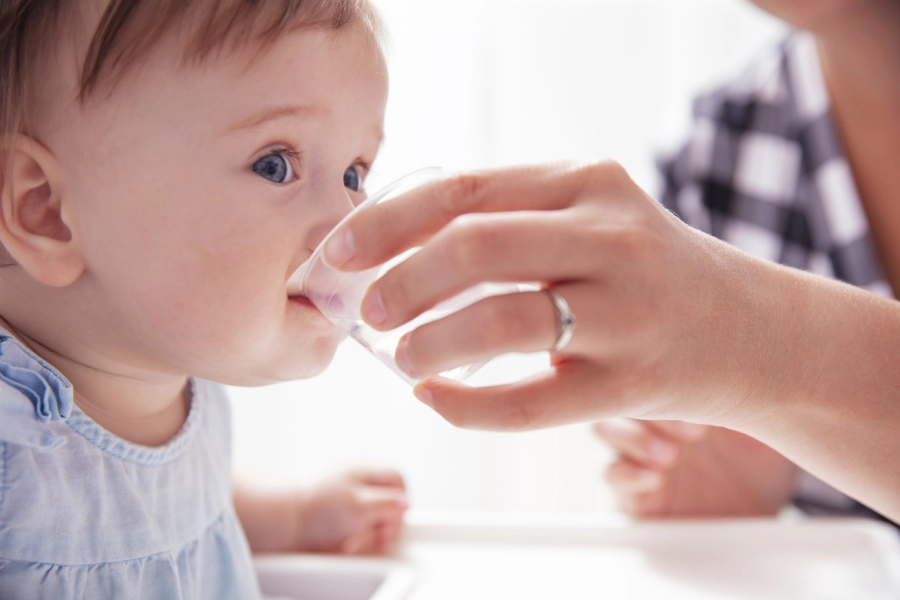 A 6 month old baby can drink from an open cup held by an adult