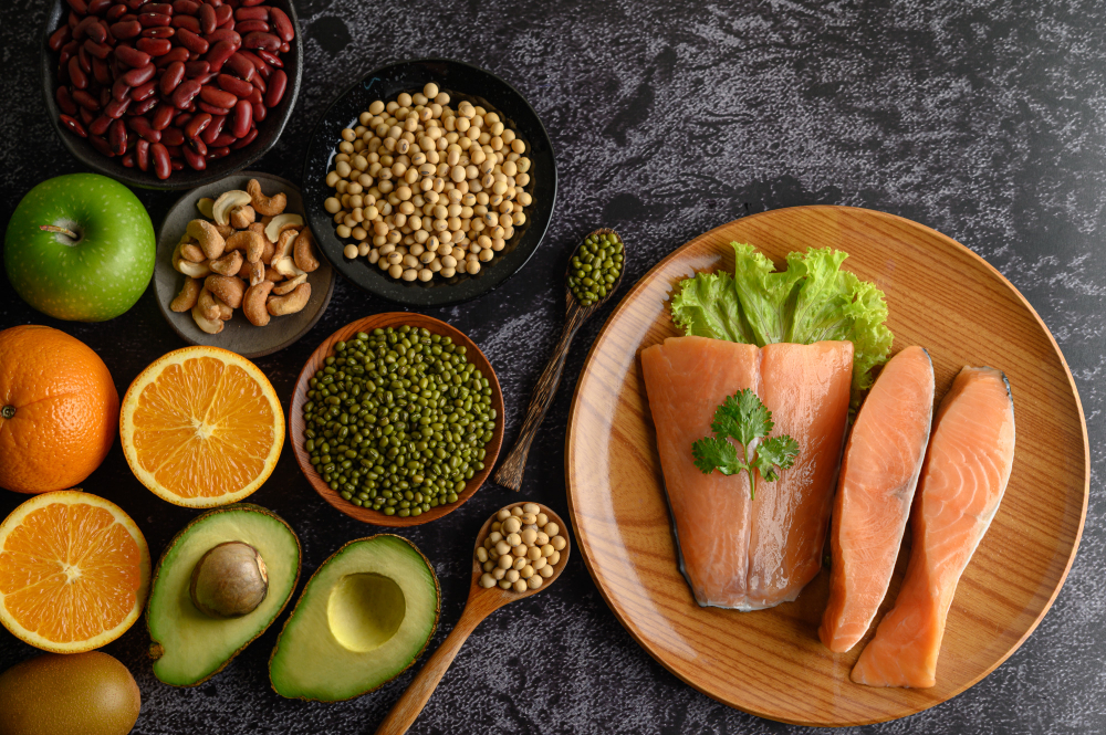A colorful flat lay of fertility-friendly foods including salmon, leafy greens, berries, avocado, nuts, and lentils